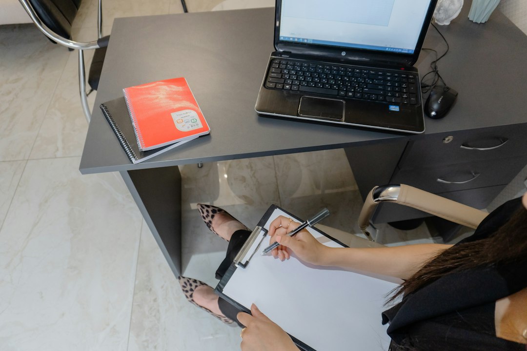Person at a desk with a laptop and clipboard, reviewing a list of hyperlinks from a Word document