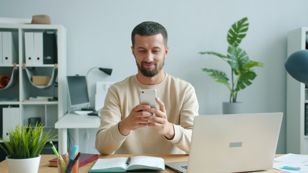 Man at an office desk using his phone, switching between work and personal accounts