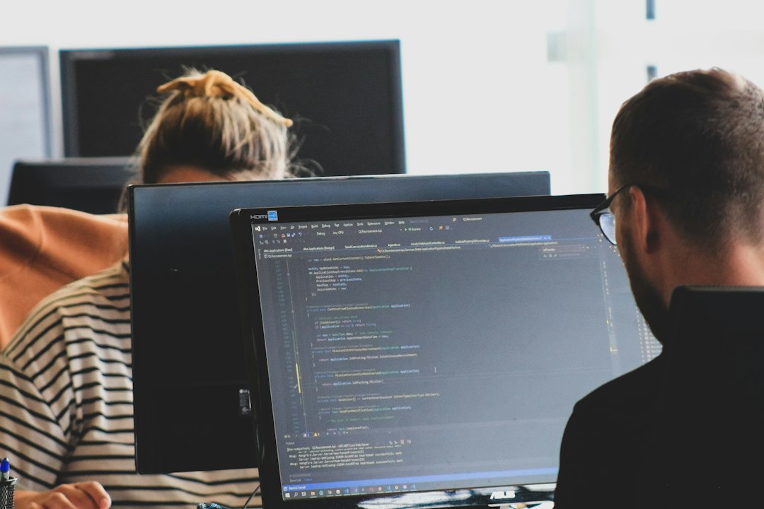Two people working at monitors in an office, opening Group Policy Management after installing RSAT