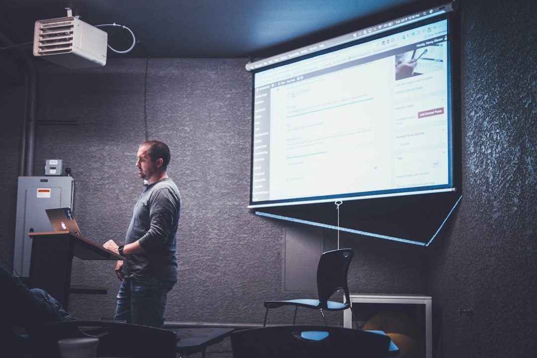 Speaker at a lectern presenting slides, with Presenter View showing notes on their own screen